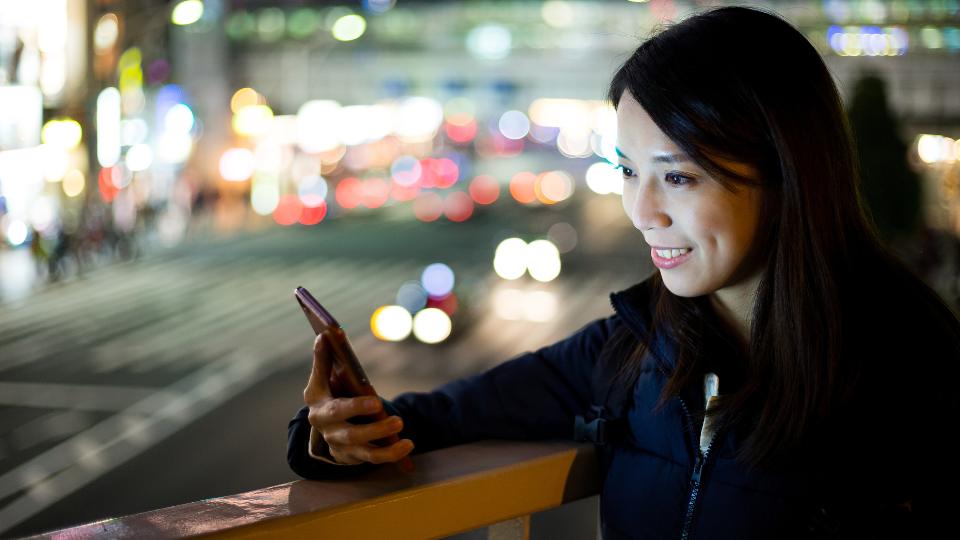 夜の街でスマートフォンを操作する女性。待ち合わせの連絡に使うイメージ
